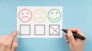 Persona marca la opción positiva en una encuesta de satisfacción laboral con caras que representan distintos niveles de satisfacción.