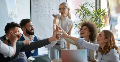 Equipo de trabajo celebrando un logro y sosteniendo un trofeo en señal de reconocimiento laboral.