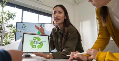 Profesional mostrando en una tablet una presentación sobre pilares ESG durante una reunión laboral, mientras explica estrategias de sostenibilidad al equipo.