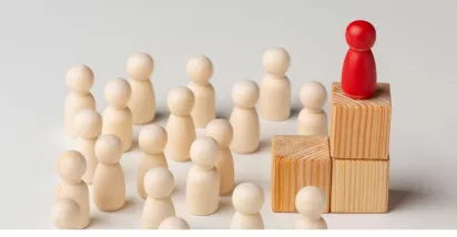 Figura roja destacada sobre bloques de madera frente a un grupo de figuras claras, representación visual de los tipos de liderazgo empresarial y la influencia del líder en el equipo.