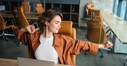 Mujer estirándose en una oficina moderna, representando bienestar laboral y equilibrio en el trabajo.