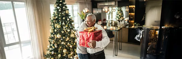 Foto muestra a un nieto regalándole un presente a su abuelo en la fiesta de Navidad.
