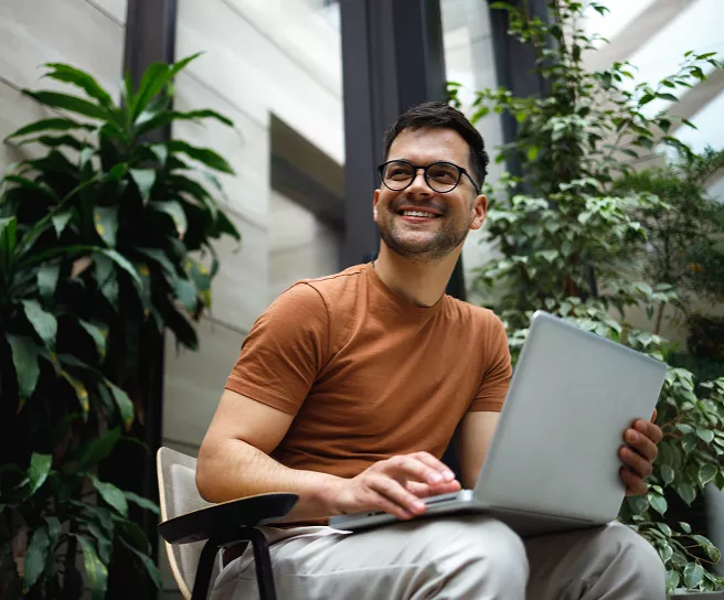 Profesional utilizando computadora portátil en un espacio moderno con áreas verdes, representando productividad, trabajo flexible y gestión digital de beneficios.
